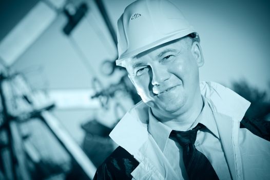 Worker in uniform and helmet on of background the metal structures, piping and sky. Look into the camera. Toned.