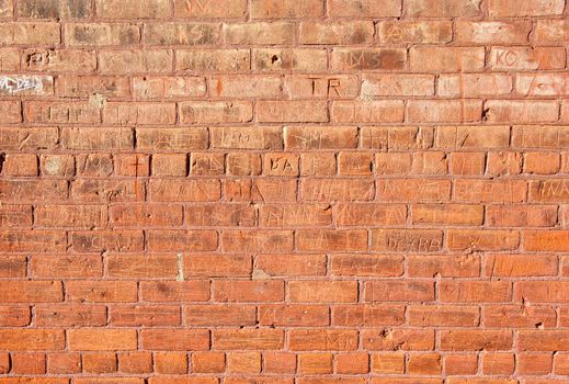 An old, red brick wall that has had many names carved into it.