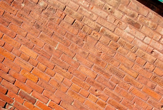 An old, red brick wall that has had many names carved into it.