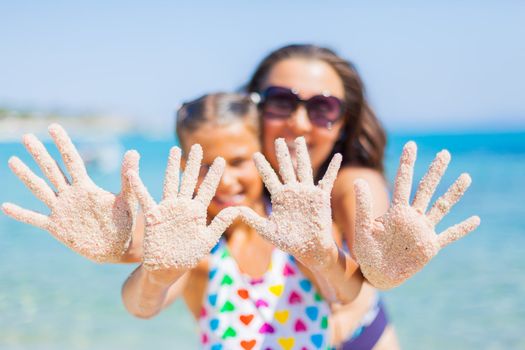 Summer beach - mother with her daughter playing on sandy beach. Focus on the hand