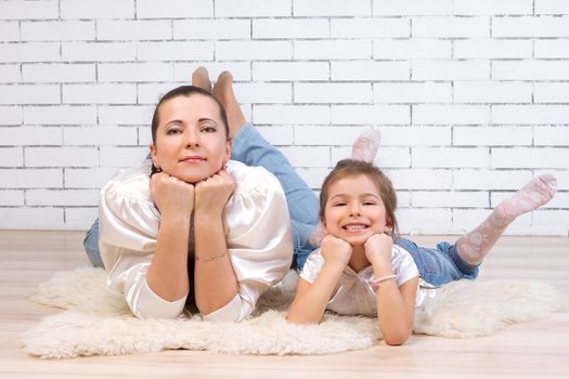 Mom with 5 year old daughter in a similar dress lying on the floor near the brick wall