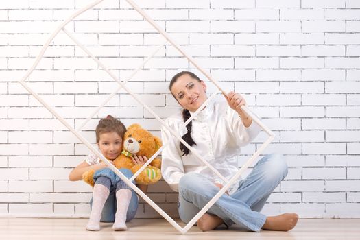 Mother and 5 year old daughter sitting by the wall, holding a toy and frame