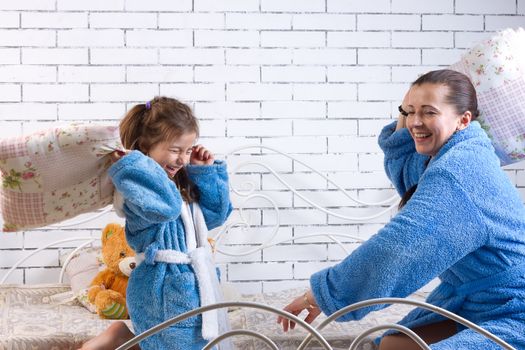 Mom and daughter in the same blue terry robes beat pillows