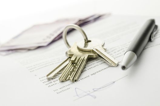 Keys of a new house on a signed contract of house sale with money in background. Concept of closed deal.