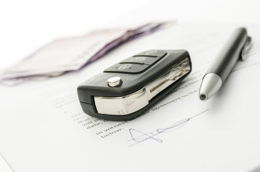 Black car key and money on a signed contract of car sale.  Focus on a key.