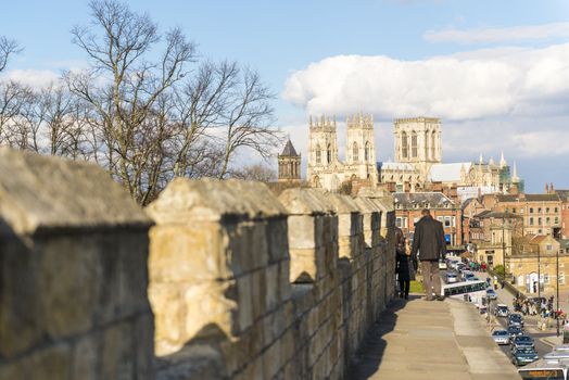 YORK, UK - MARCH 30: Pedestrians walking on the mediaeval wall that surrounds the city, with York Minster in the background. March 30, 2013 in York.