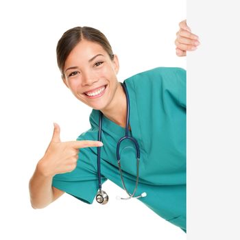 Medical sign person - woman showing blank poster billboard placard pointing. Young female nurse or medical doctor professional in green scrubs smiling happy isolated on white background.