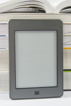 Electronic book reader with blank screen and pile of books 