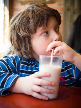 Young boy drinking a glass of milk with a straw in a restaurant