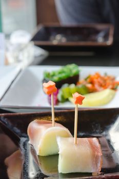 Salmon and fruit sticks with  melon on black dish