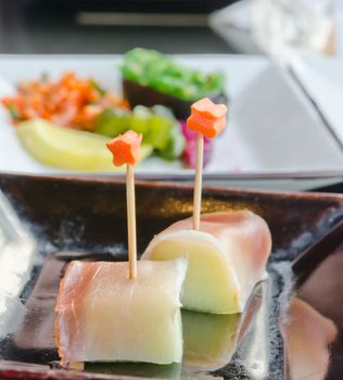 two pieces of salmon and fruit sticks with  melon on dish