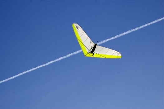 Hang Glider centre against deep blue sky with a white vapour trail criss-crossing image, with copy space.