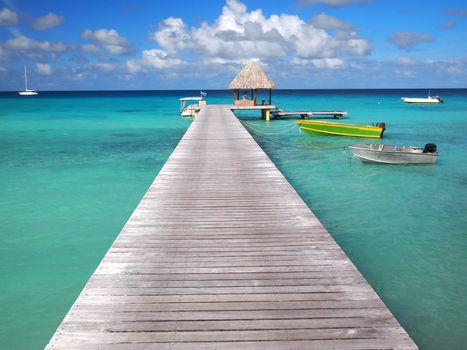 Boats attached to a pier and a thatched hut inside the tropical lagoon of the pacific atoll Rangiroa, an island of the Tahiti archipelago French Polynesia.
