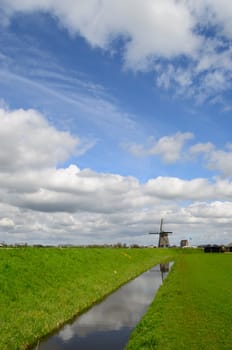 Dutch clouds in the sky over a windmill, a meadow, a ditch and a dike in Holland.