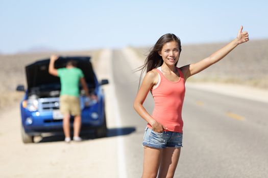 Car breakdown problems - woman hitchhiking thumbing while man tries to fix car. Young couple need auto service help on interstate highway in California, United States. Asian woman model.