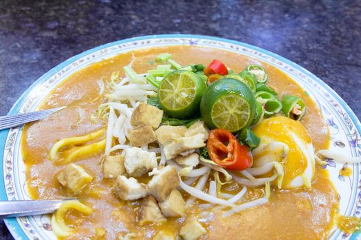 Malay Mee Rebus Noodle Dish Garnished with Cut Chili Peppers Tofu Chinese Celery and Hard Boiled Egg Closeup