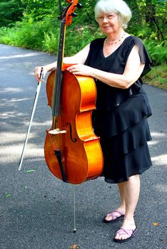 Female cellist posing with her cello outside.