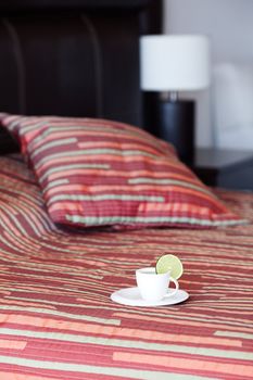 bed with a pillow, a cup of tea on the bedside table and lamp