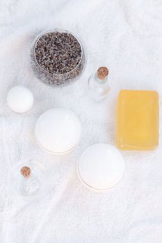 cosmetic containers, bottles, soap and lavender on a white towel