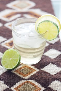 water with lemon and lime in a glass with ice on ethnic mat