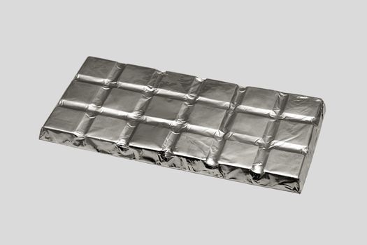 Chocolate bar packed in silvery foil, isolated on a gray background.