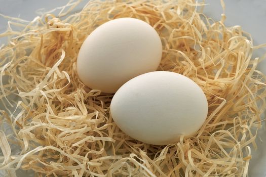 A pair of white chicken eggs lying on straw, close-up.