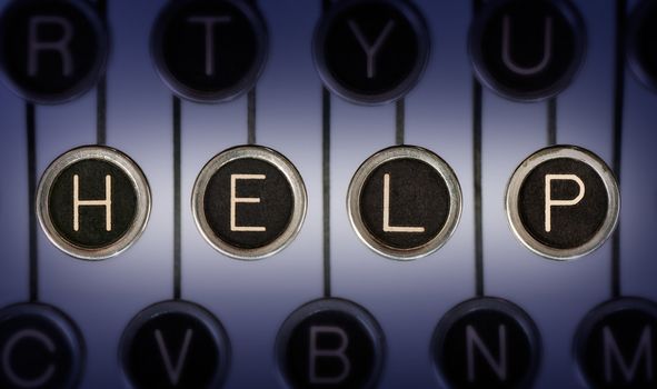 Close up of old typewriter keyboard with scratched chrome keys that spell out the word "HELP". Lighting and focus are centered on "HELP". 