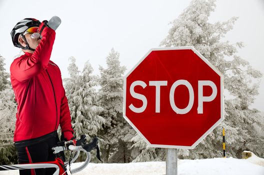 Cyclist on road bike near a stop sign in the mountains with snow.