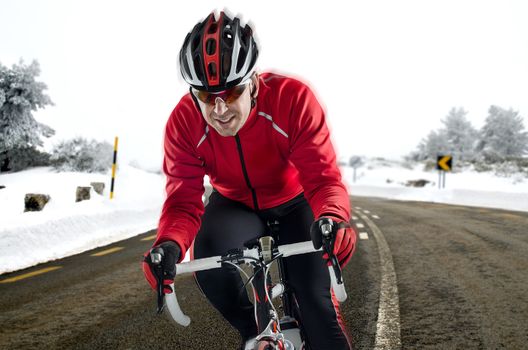 Cyclist on road bike through a asphalt road in the mountains with snow.