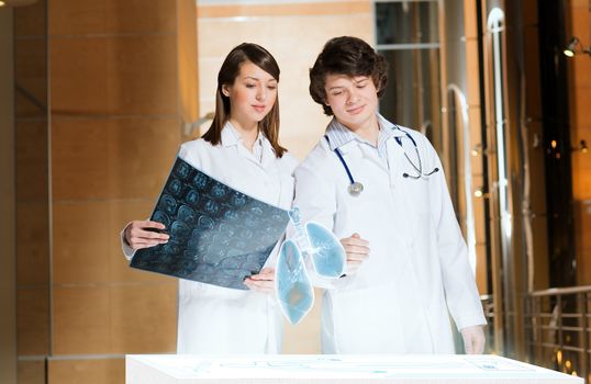 two doctors stand near glowing table discussing. projected objects on a desk