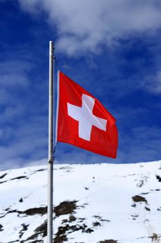 Swiss flag in the Alps mountains by beautiful cloudy day