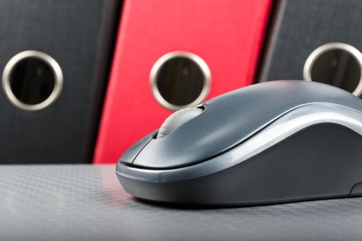 A wireless mouse placed on notebook and three folders in the background