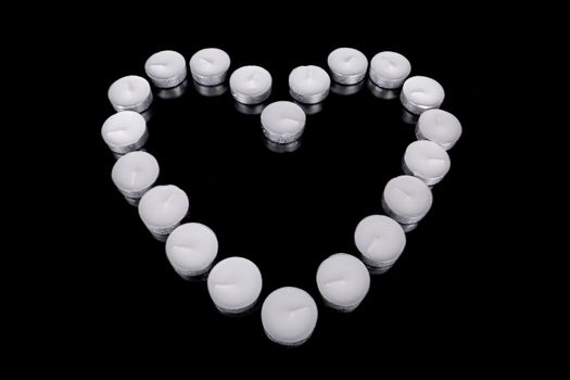 Group of white candles forming a heart  on black isolated background. Concept for St. Valentine