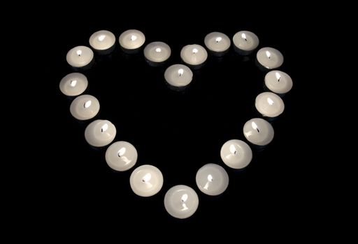 Group of burning candles forming a heart  on black isolated background. Concept for St. Valentine