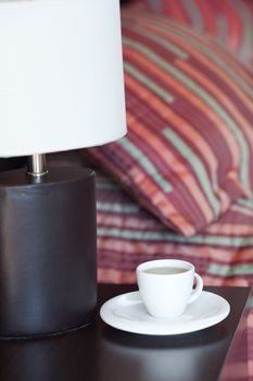 bed with a pillow, a cup of tea on the bedside table and lamp