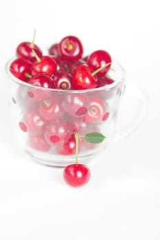 cherry with green leaf and a cup of cherries on a white background