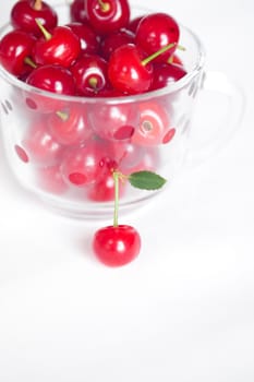 cherry with green leaf and a cup of cherries on a white background