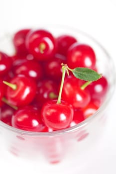 cherry with green leaf and a cup of cherries on a white background