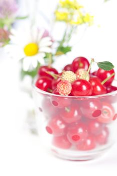 glass cup with cherries and wild strawberries and a bouquet of wildflowers