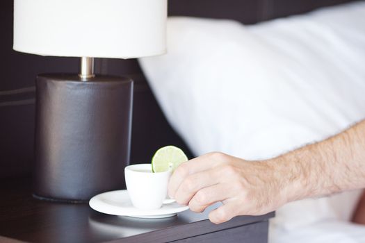 man hand, a cup of tea on the bedside table and lamp