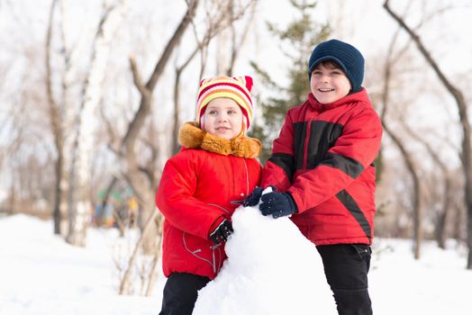 Boy and girl playing with snow in winter park, spending time together outdoors