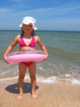 The little girl with inflatable circle on the sand at the sea