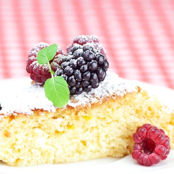 cake with icing, raspberry, blackberry and mint on a plate on plaid fabric