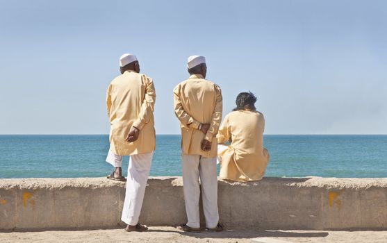Dwarka Roadtrip. Horizontal portrait of three clerics in formal attire looking  out to the horizon of the Arabian Sea. The location of this conceptual shot was at the beach and promanade at Dwarka, Gujarat, India near the Krishna Temple.