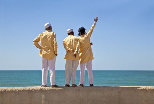 Horizontal portrait of three clerics in formal attire looking and pointing out to the horizon of the Arabian Sea. The location of this conceptual shot was at the beach of Dwarka Bay, Gujarat, India near the Krishna Temple.