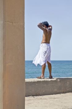 Hindu priest shading his eyes looking to the horizons of the Arabian Sea towards the sun at Dwarka beach and promenade in Gujarat, India