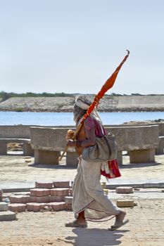 Vertical capture of a religious hindu man holy man walking, carrying a flag from his pilgrimage to the Krishna Temple at Dwarka in Gujarat India