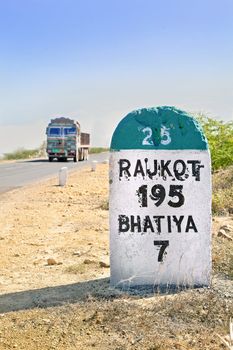Dwarka Roadtrip. Vertical take of 195 kilometer milestone and direction sign to Rajkot in Gujarat India with a typical truck about to pass by. Rural country side location in the summer season with dry barren wasteland of the region