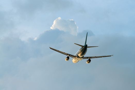 Back view of airplane flying in cloudy sky