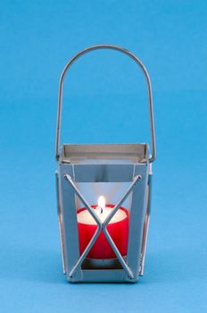 steel grey retro candlestick with handle and red candle burn on blue background.